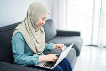 Female muslim woman using laptop while holding credit card.