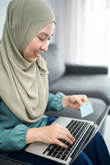Female muslim woman using laptop while holding credit card.