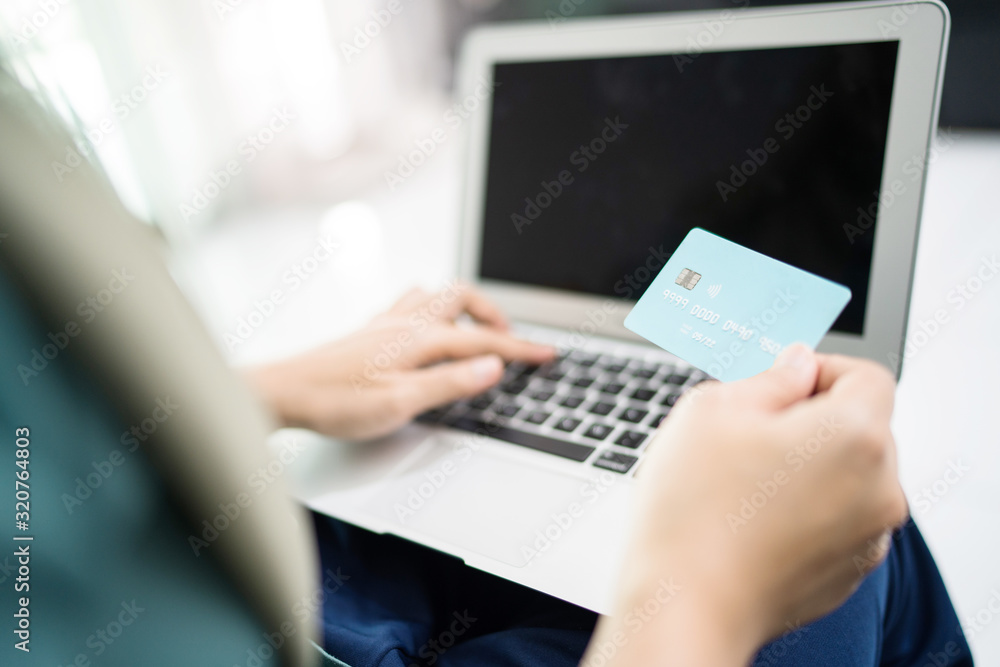 Wall mural Female muslim woman using laptop while holding credit card.