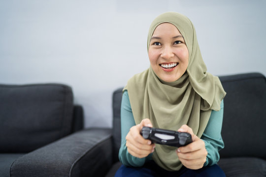 Beautiful muslim woman playing console games at her couch.