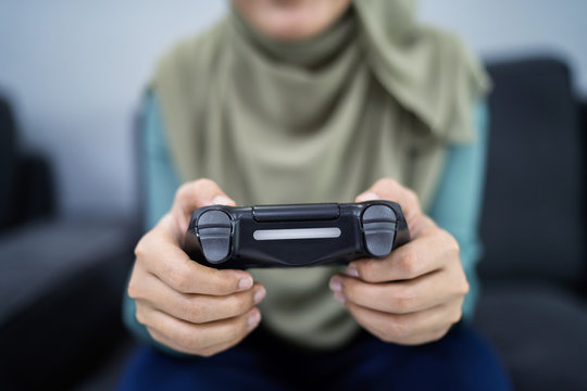 Beautiful muslim woman playing console games at her couch.