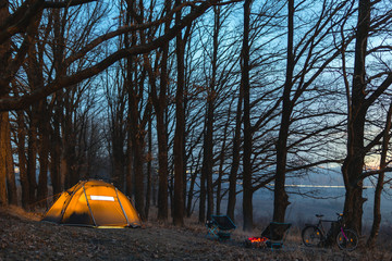 Night camp in the forest. light in the camping tent and portable chairs and aluminum table. Cold autumn. concept of vacation and outdoor activities. without people. copy space. bonfire and bicycle.