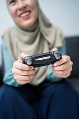 Beautiful muslim woman playing console games at her couch.