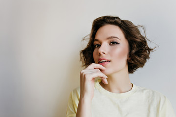 Close-up indoor portrait of lovely girl with dark hair. Studio shot of graceful pale young woman with short haircut isolated on white background.