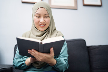 Muslim woman reading a book at her living room.