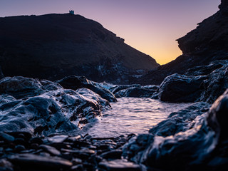 Fototapeta premium Purple and orange sky at Boscastle in North Devon. Taken down low by the shiny rocks.