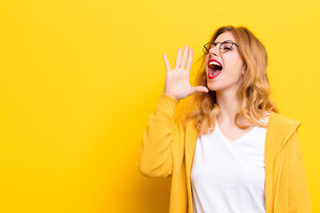 young pretty blonde woman yelling loudly and angrily to copy space on the side, with hand next to...