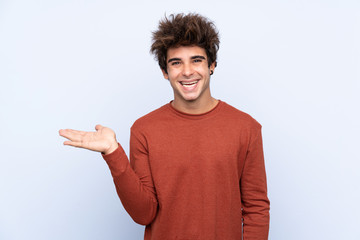 Young caucasian man over isolated blue background holding copyspace imaginary on the palm to insert...