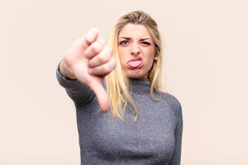 young pretty blonde woman feeling cross, angry, annoyed, disappointed or displeased, showing thumbs...