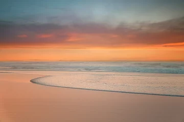 Fotobehang prachtige zonsondergang op het strand met een golf op de kust © mimadeo