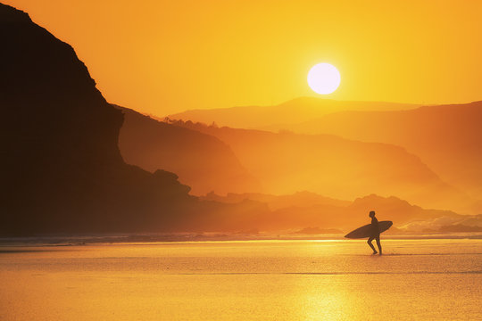 surfer exiting water at misty sunset
