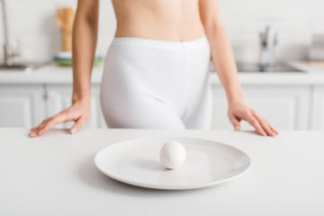 Obraz na płótnie Canvas Selective focus of egg on plate and fit woman near kitchen table