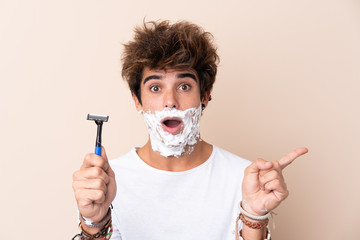 Young handsome man shaving his beard surprised and pointing side