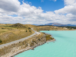 Stunning aerial high angle drone view of State Highway 8 leading along the shores of Lake Pukaki, an alpine lake on New Zealand's South Island. The water is famous for its distinct bright colour.