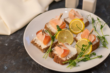 Sandwiches with salmon on dark bread, spread with cheese sauce. The meat is wrapped in a slice of daikon and fixed with a decorative clothespin. On a wooden background.