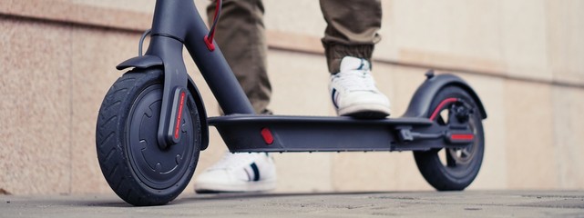 Young man with modern electric scooter on blurry city street background.