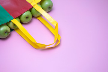 Closeup of green apples in multicolor reused plasti bag.  Recycled bag campaign advertising and healthy living concepts. magenta background.