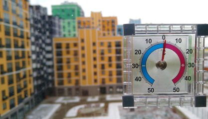 Street thermometer with a red arrow on the background of a multi-colored multi-storey building and...