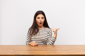 young pretty woman looking astonished in disbelief, pointing at object on the side and saying wow,...