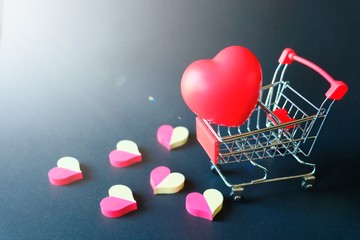 Red rubber heart in small shopping cart with many two tone red and white placed spread on black...