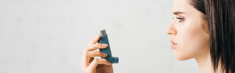 Side view of young woman holding inhaler on white background, panoramic shot