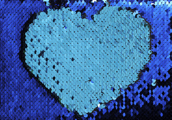 Carved paper heart on blue sequins texture.