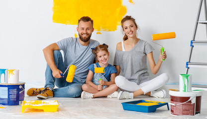 Repair in apartment. Happy family mother, father and child daughter  paints wall