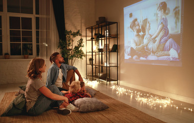 family mother father and children watching projector, TV, movies with popcorn in   evening   at...