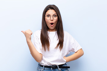 young pretty woman looking astonished in disbelief, pointing at object on the side and saying wow,...