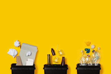 Paper, glass, plastic in black containers on a yellow background. The concept of separate...