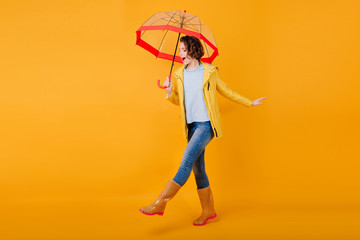 Glad curly girl in jeans funny dancing holding trendy parasol. Studio portrait of inspired young...