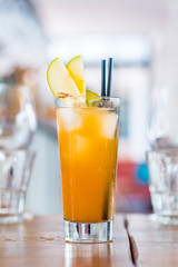 Close-up of orange fresh fruit cocktail drink in a tall glass decorated with apple.