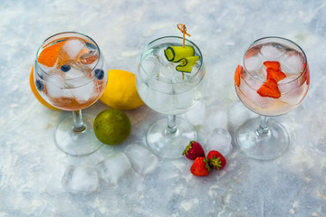Three gin tonic cocktails with strawberries, lime and blueberries.