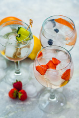 Close-up of three gin tonic cocktails with strawberries, lime and blueberries.