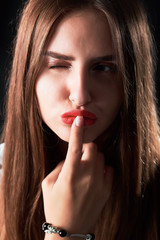 Naklejka premium Close-up studio portrait of a young girl with long hair and finger on red lips.