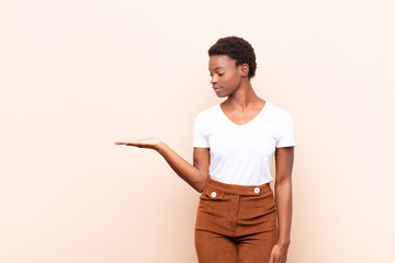 young pretty black womanfeeling happy and smiling casually, looking to an object or concept held on...