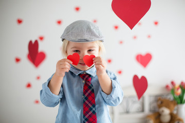 Cute blonde toddler boy, holding heart toy and playing with hearts for Valentine