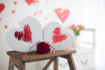 Box in a shape of heart, flowers, red roses and red paper hearts in a Valentine decorated room