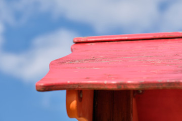 Abstract detail of a red wooden roof with the paint flaking off on a playground against the bright blue sky with clouds. Seen in Germany in March 2019