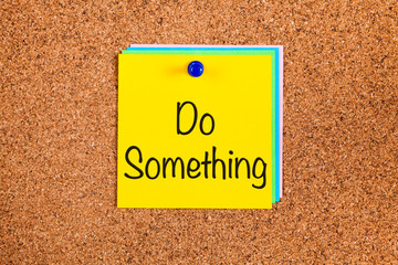 Post-it notes with words Do Something on corkboard.