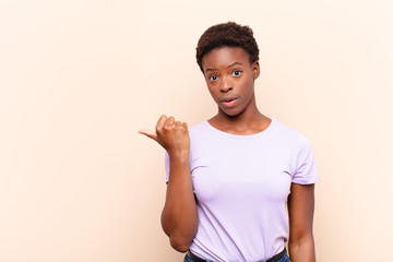 young pretty black womanlooking astonished in disbelief, pointing at object on the side and saying...