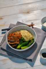 Yellow noodle on top with roasted chicken and green vegetable placed on the white wood table. 