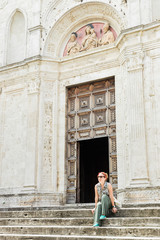Fototapeta na wymiar Young female traveler sitting on church steps in old town in Tuscany, Italy