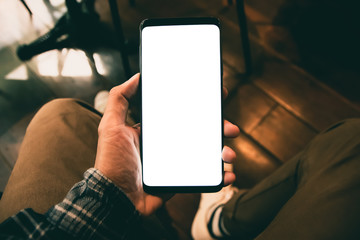 Asian man sitting on the chair in hand holding smartphone use cell phone white screen blank copy space for your text message in cafe with light Sunset, Vintage tone. Selective focus