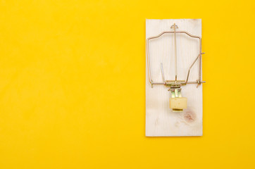 Mousetrap with cheese on a yellow background with copy space