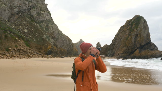 A traveler takes pictures with a modern camera of landscapes on the ocean shore among rocks and large waves