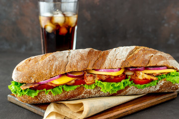 A sandwich of dark bread with salad, bacon, tomatoes, cheese and onions. Breakfast. Fast food.