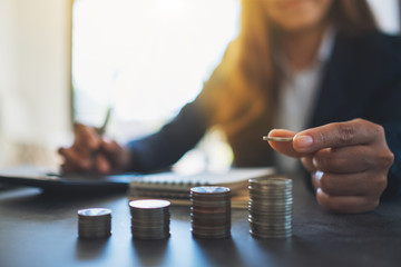 Businesswoman holding and stacking coins while calculating money on the table