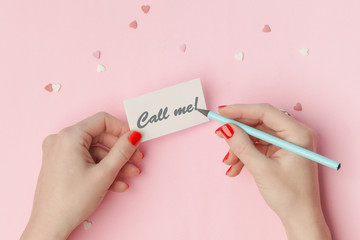 Top view of female writing call me note on a pink background, Valentine's day concept