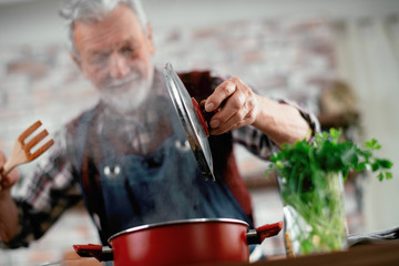 Old man in kitchen. Senior man cooking delicious food. 